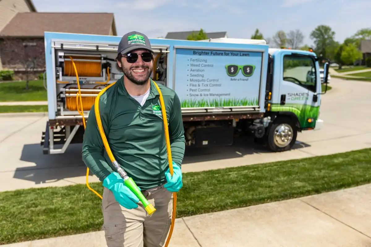 Smiling Shades of Green technician holding a treatment hose beside a service truck
