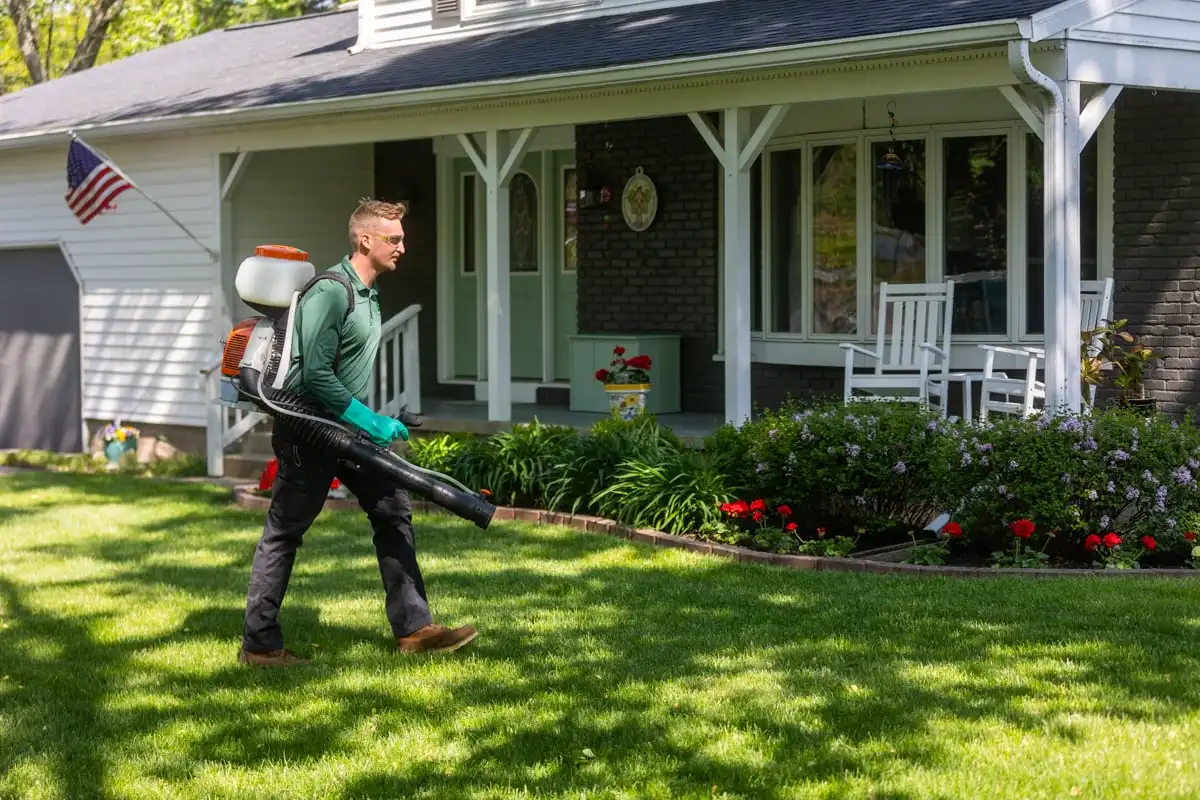 Technician carrying a backpack mister across a residential lawn
