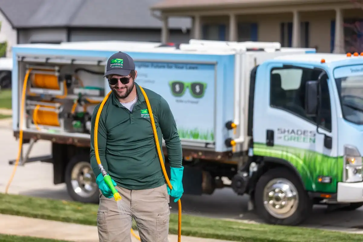Technician holding a liquid-treatment hose beside a Shades of Green service truck