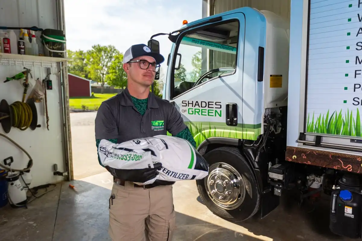 Shades of Green technician carrying a bag of granular fertilizer