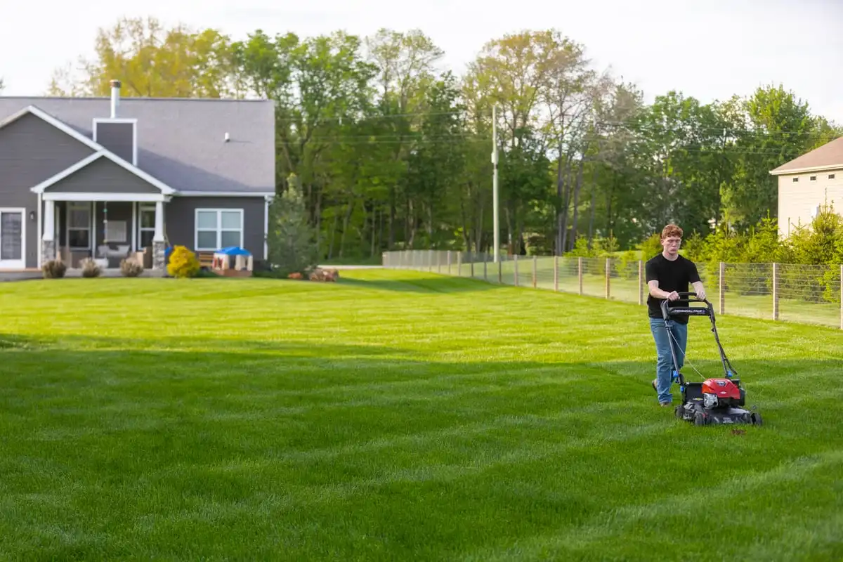 Homeowner mowing a green backyard lawn