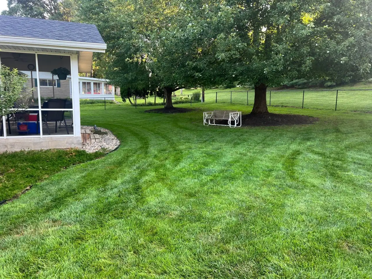 Curved mowing stripes across a backyard with a screened porch and shade trees in Attica, Indiana