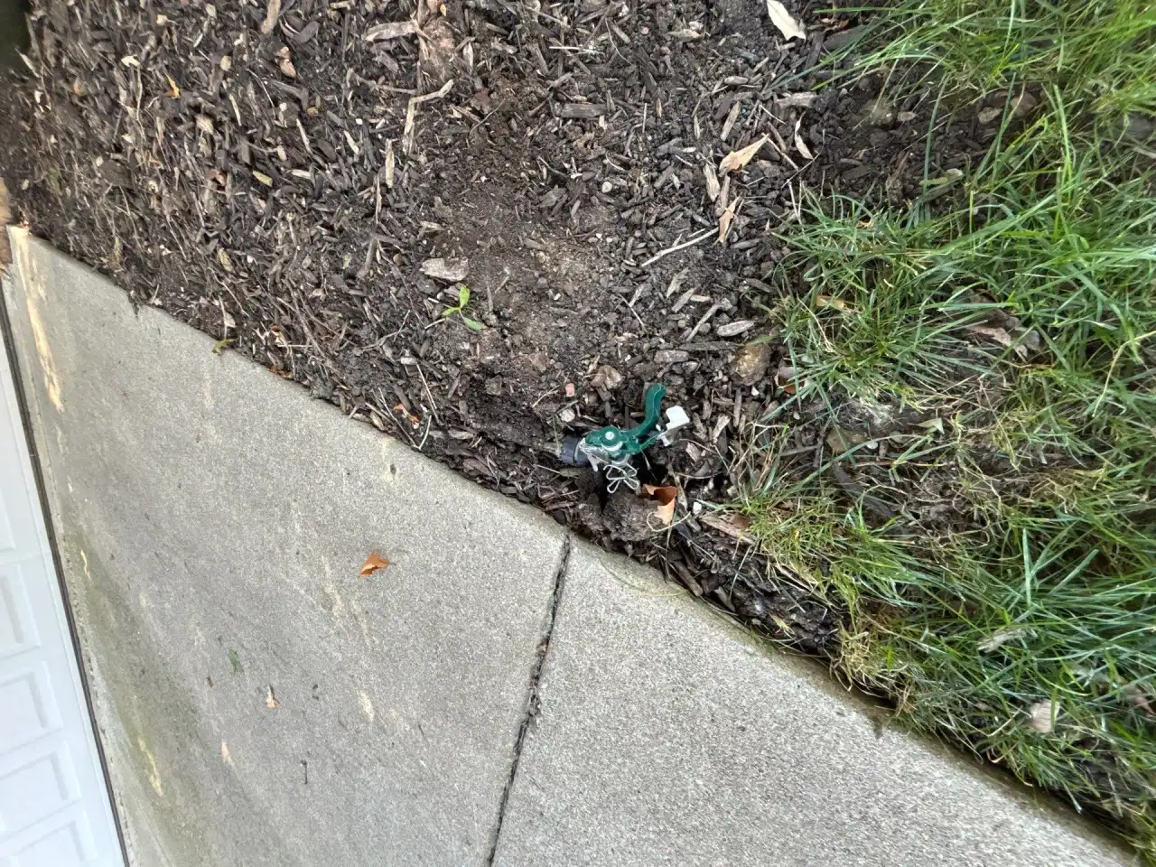 Damaged sprinkler head between a mulch bed and the sidewalk in West Lafayette, Indiana