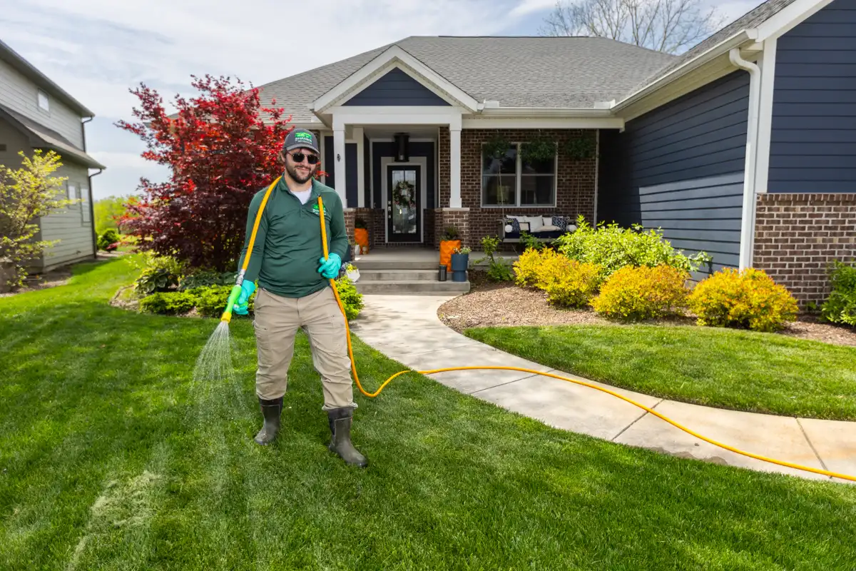 Technician in green sunglasses spraying a front lawn from a hose line