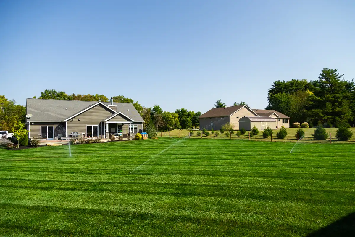 Sprinklers running across a wide, striped lawn in front of two homes
