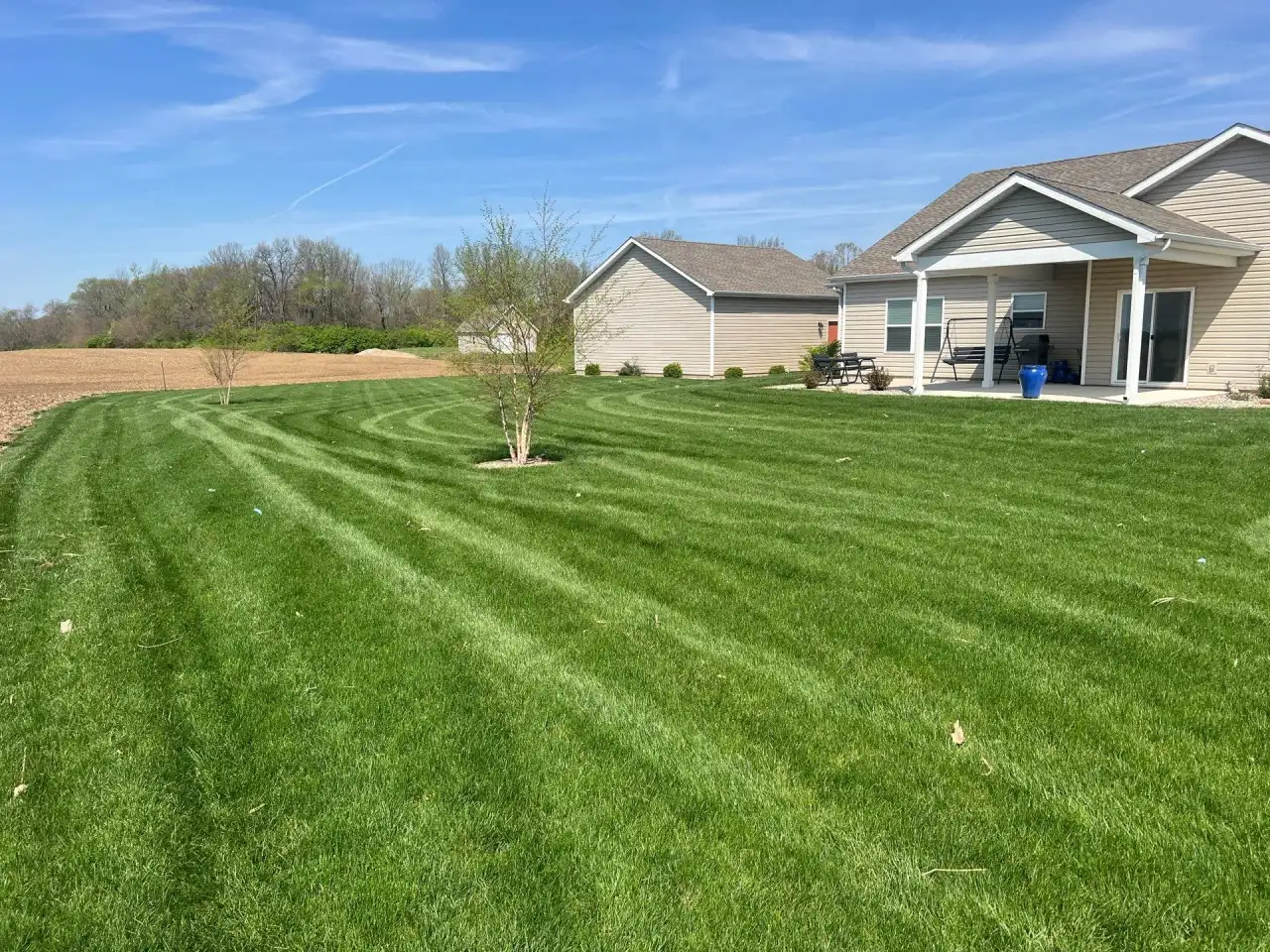 Curved stripes across a lawn behind a beige home, with a farm field beyond, in Attica, Indiana