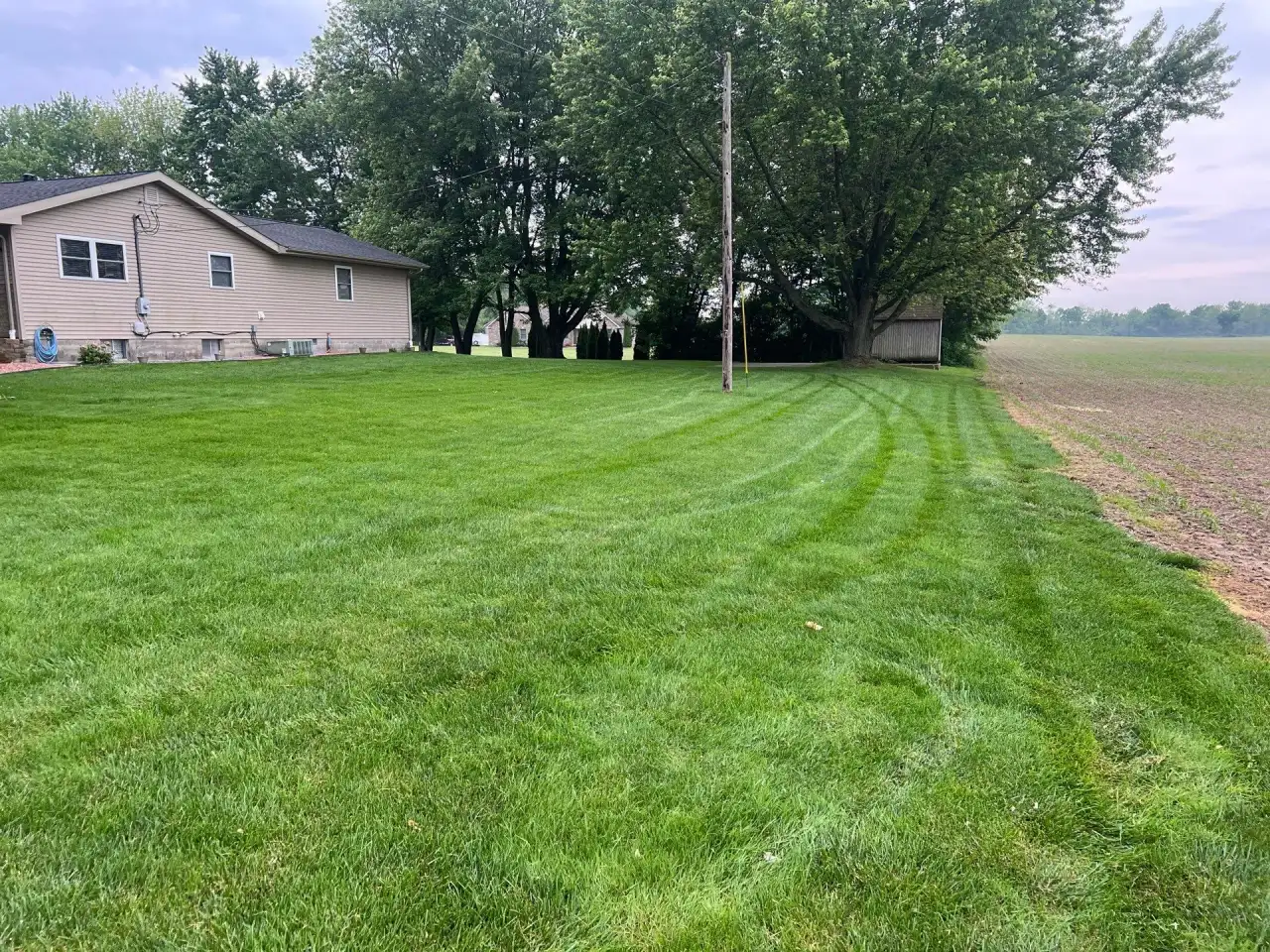 Wide striped lawn beside a plowed farm field and a ranch home in Kokomo, Indiana