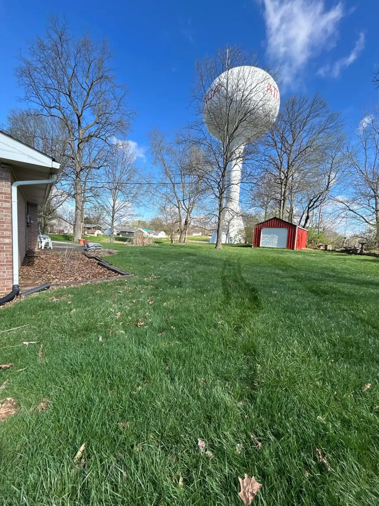 Spring lawn in Attica, Indiana, with a water tower rising behind the trees