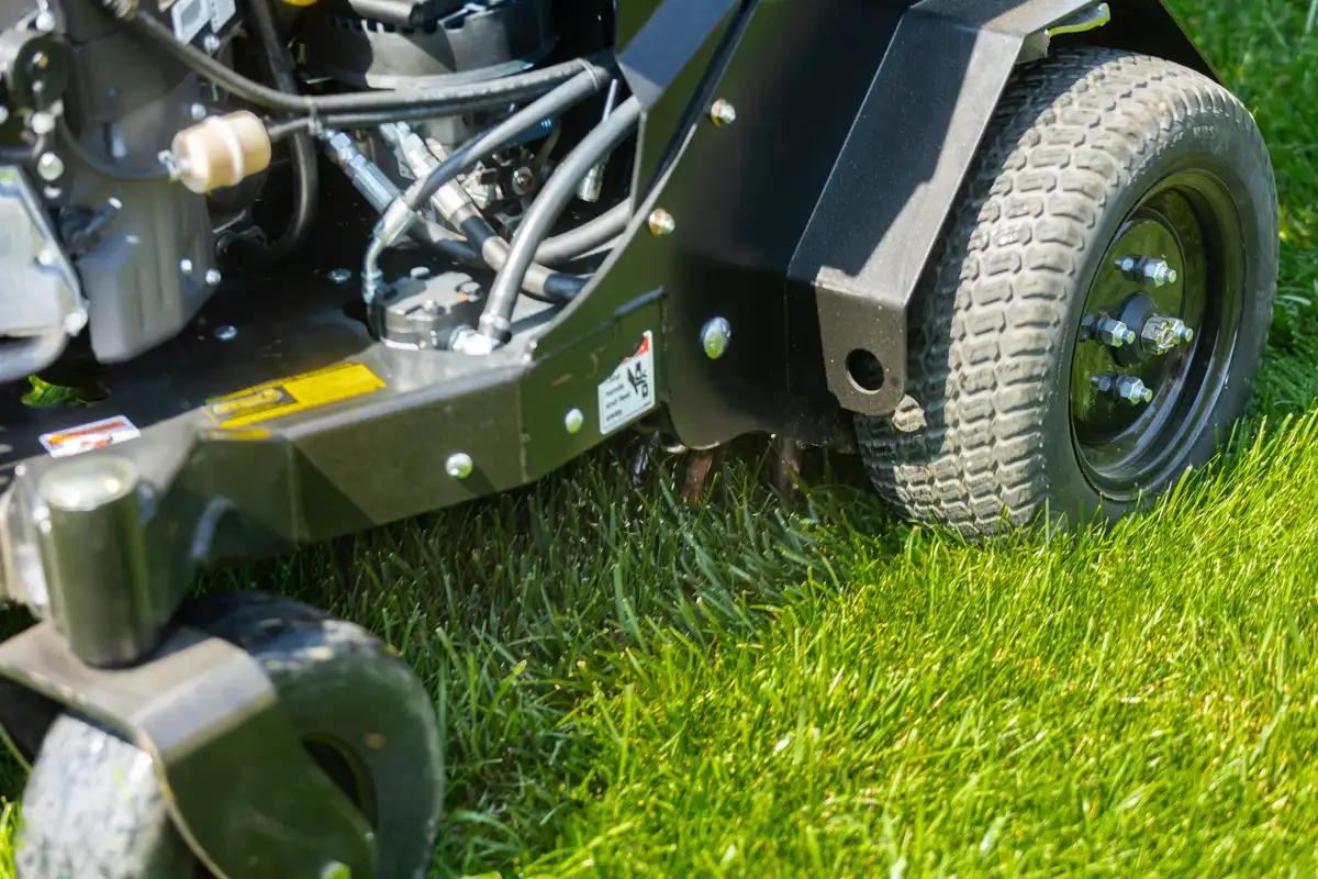 Close-up of a stand-on aerator's wheel and frame rolling over green grass