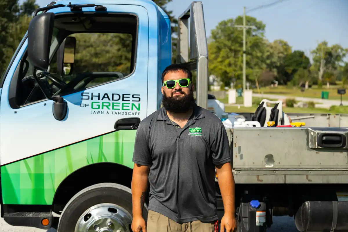 Technician in green sunglasses standing in front of a Shades of Green service truck