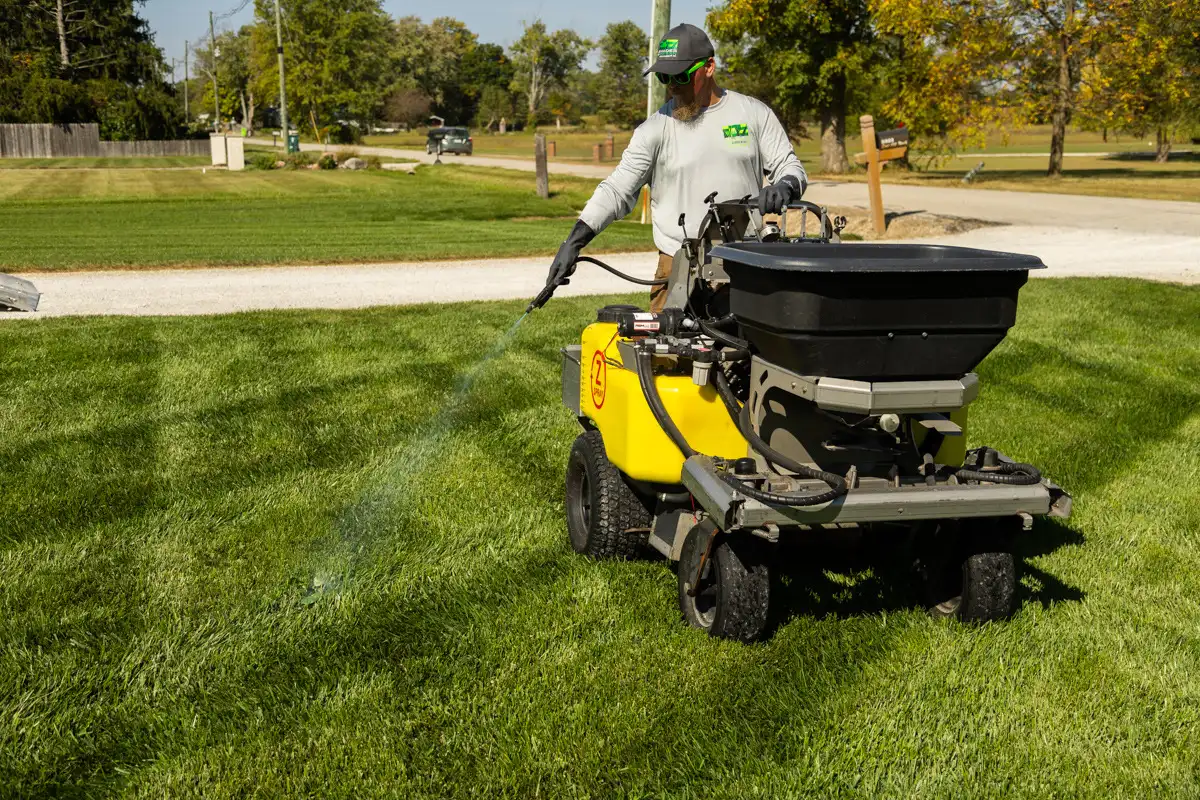 Technician on a ride-on sprayer spot-treating a lawn with a hose wand