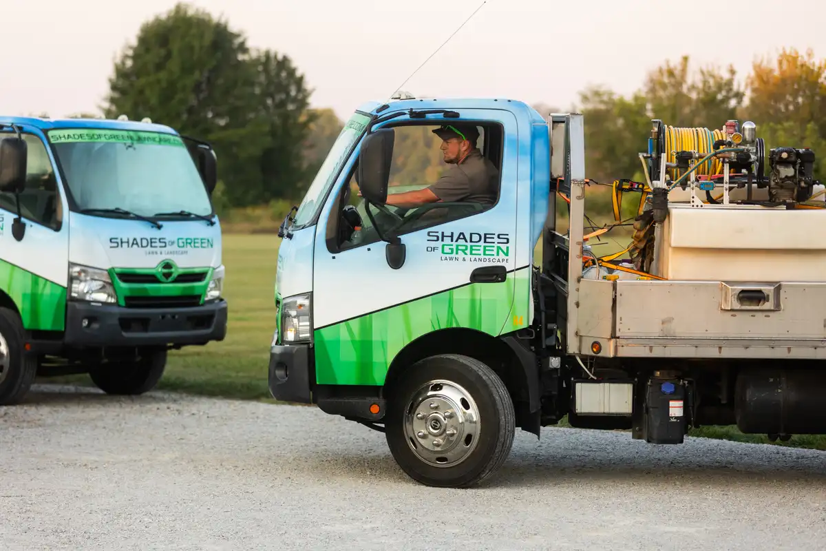 Two Shades of Green service trucks on a gravel lot, a technician at the wheel of one