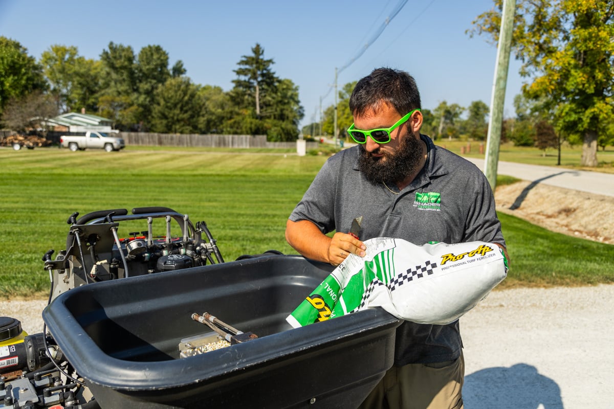 a lawn care technician loads his hopper with granular slow-release fertilizer