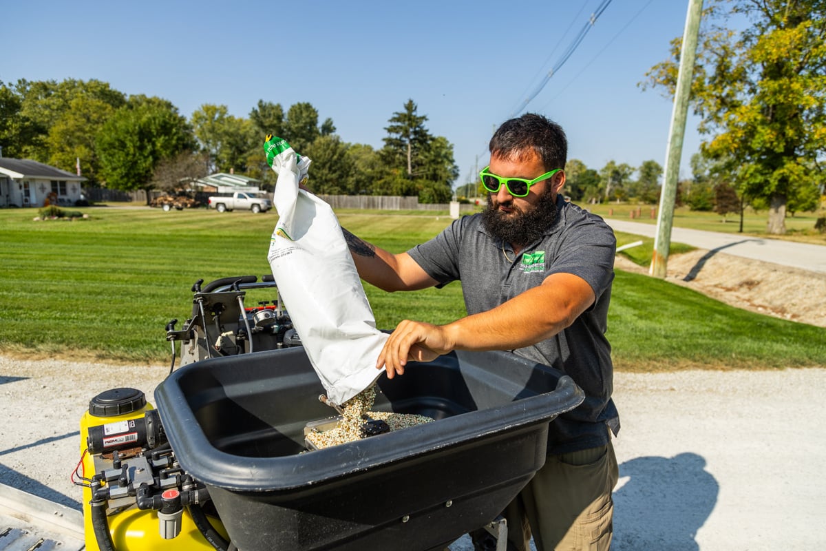 lawn care technician loading his hopper with granular fertilizer