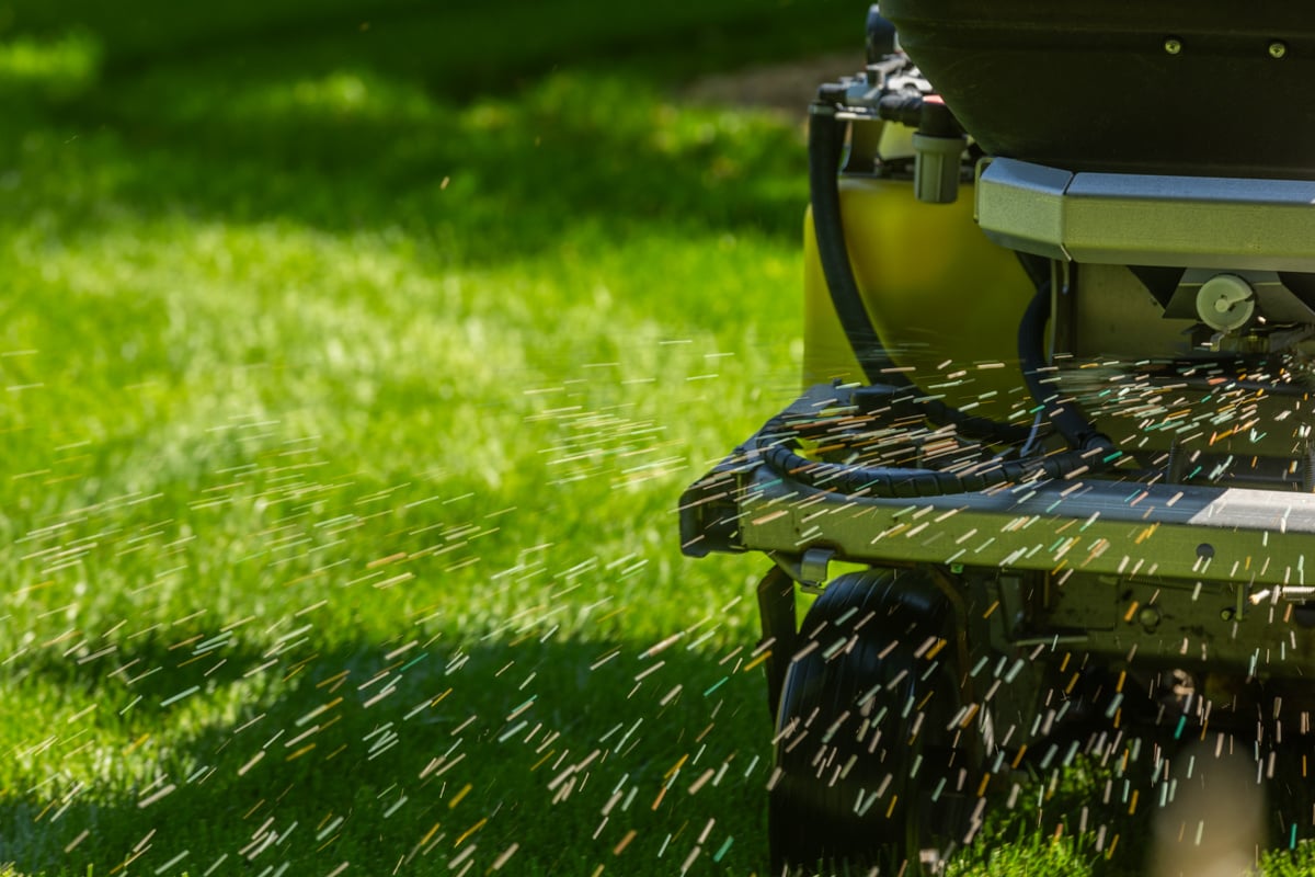 close up of slow-release granular fertilizer being applied onto grass out of a hopper